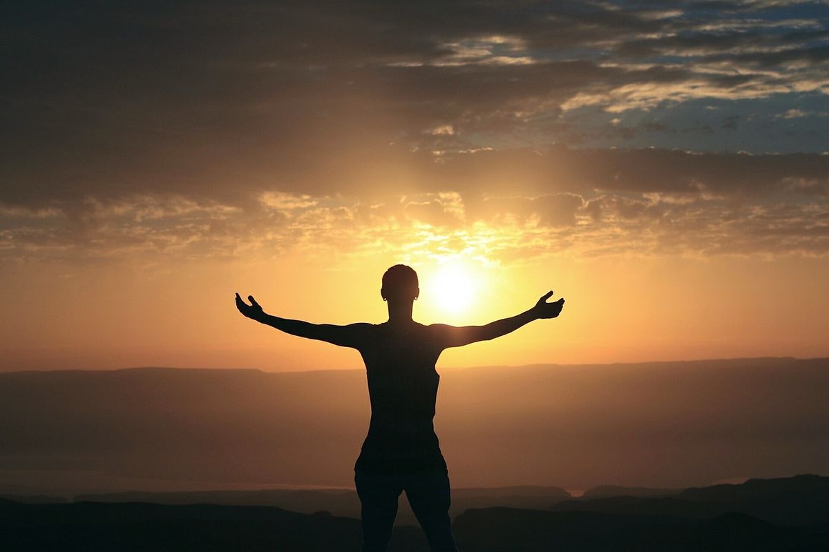 Silhouette of a person with arms outstretched facing the sunrise